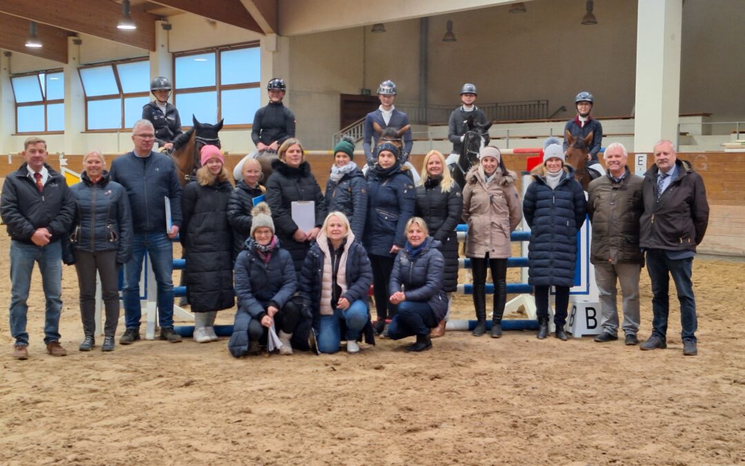 Eine Gruppe Menschen in der Reithalle. Im Hintergrund Reiter mit Pferden.