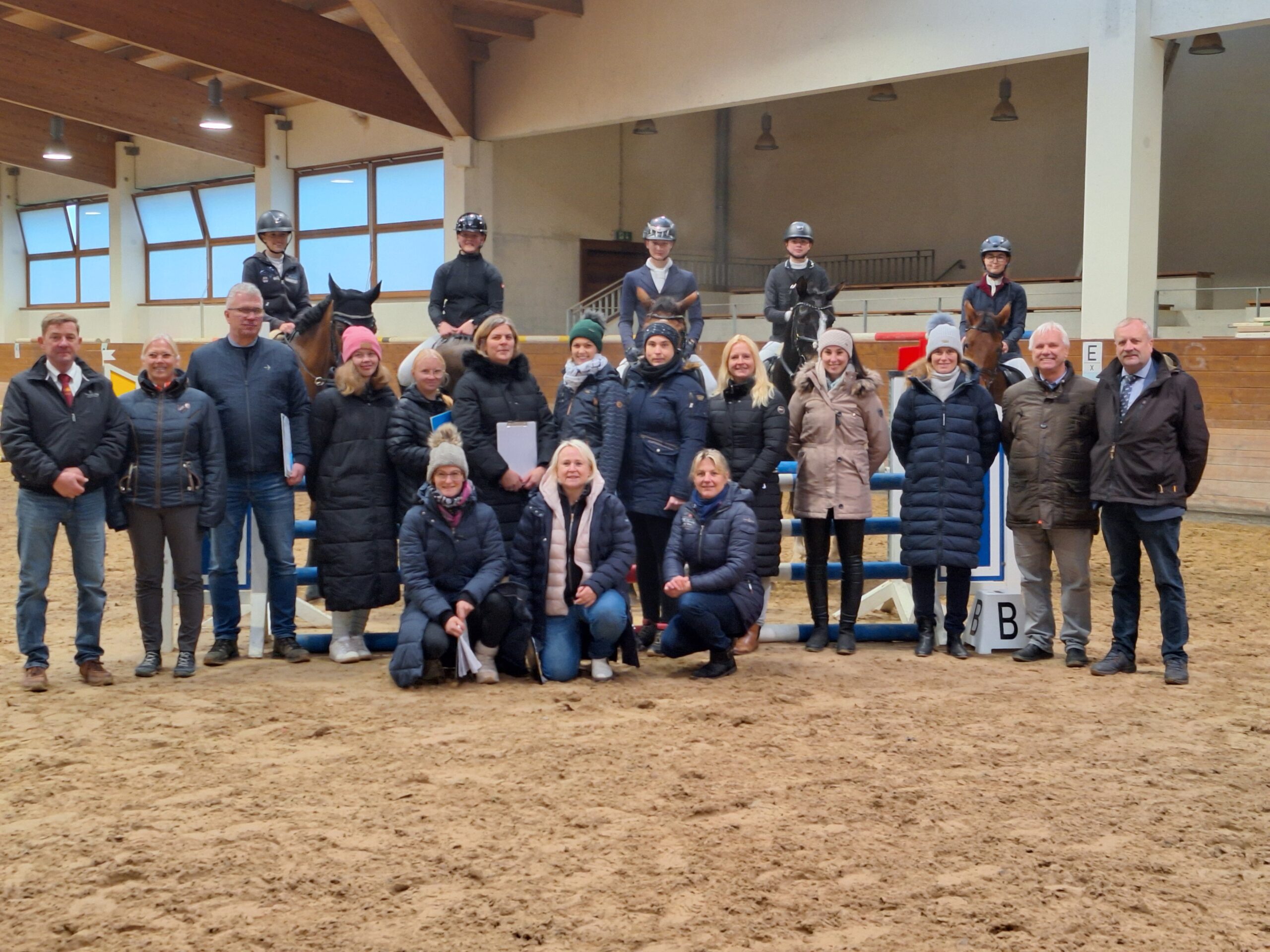 Eine Gruppe Menschen in der Reithalle. Im Hintergrund Reiter mit Pferden.